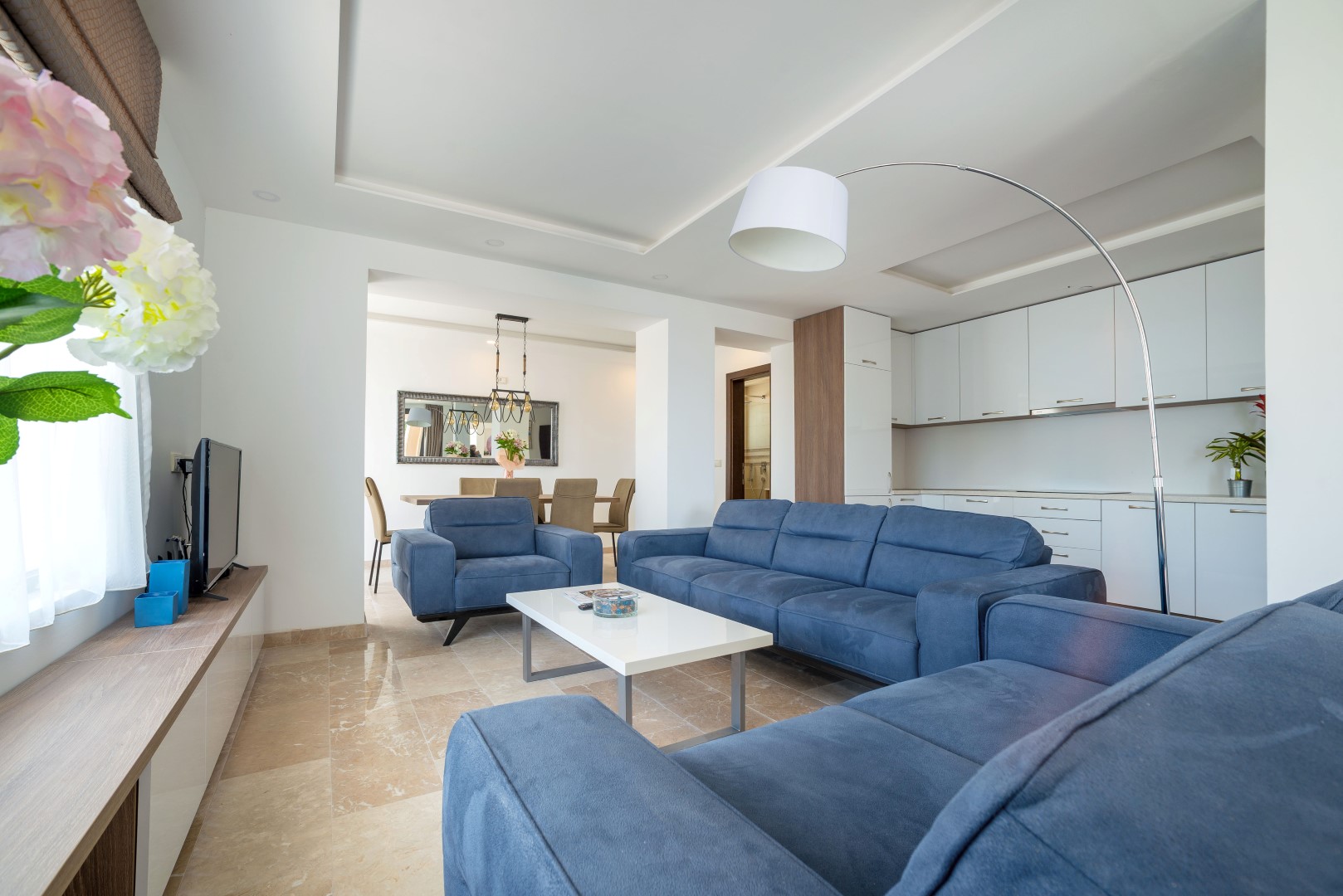 Modern living room with blue sofas and a kitchen in a villa in Bečići, Montenegro: marble floor and stylish interior.