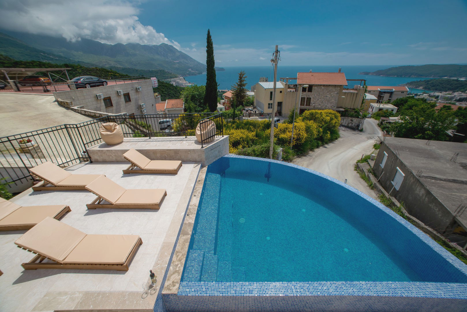 Open-air pool with sea and mountain views at a villa in Bečići, Montenegro, with a lounge area and sun loungers on the terrace.