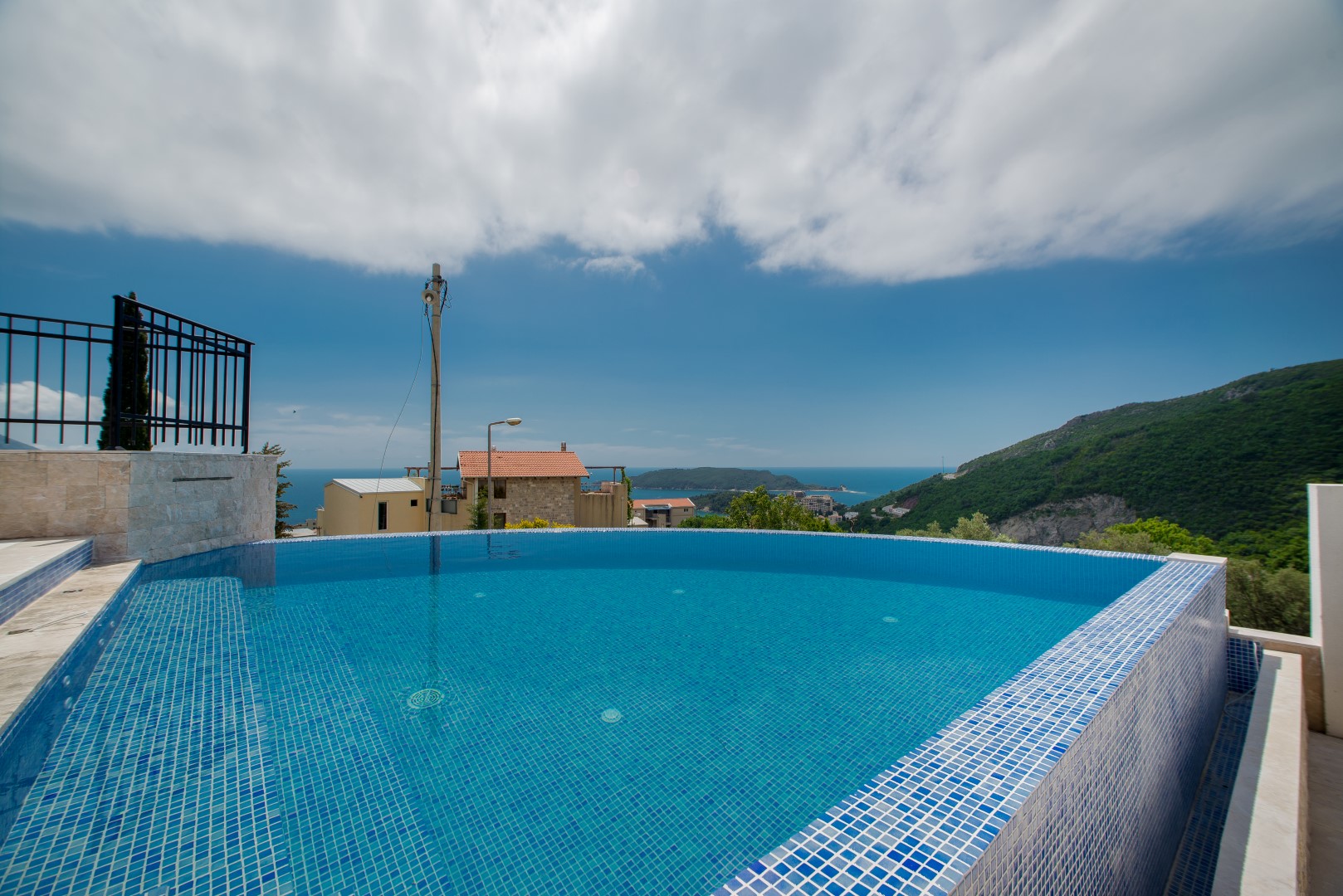 Outdoor pool with panoramic views of the sea and mountains at a villa in Bečići, Montenegro. Pool finished with blue mosaic tiles.