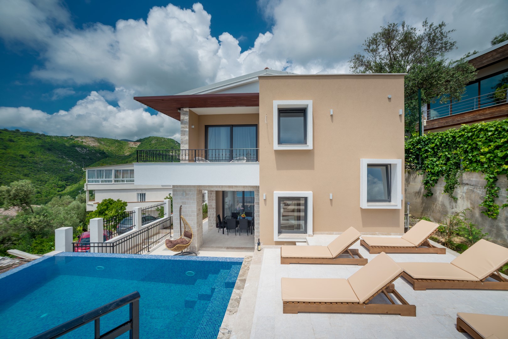 Modern villa in Bečići, Montenegro: pool, terrace with sun loungers, mountain view, and stylish facade finish.