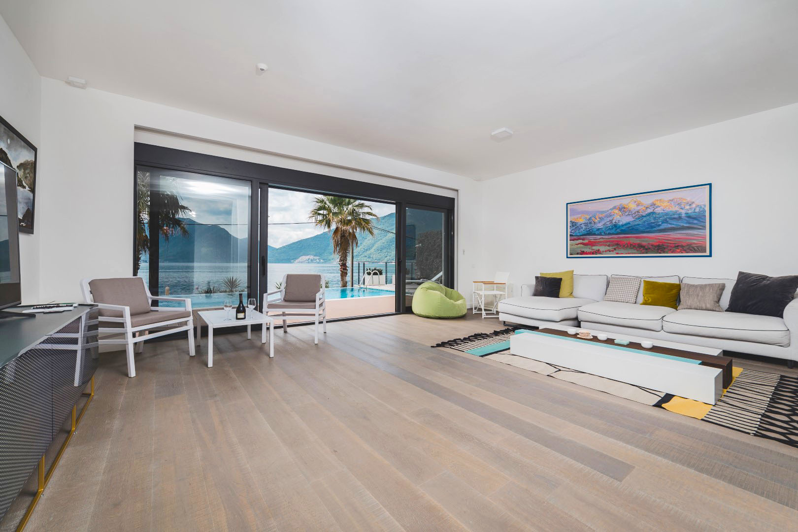 Villa living room in Strp, Montenegro: modern furniture, panoramic windows with views of the sea, mountains, and pool.