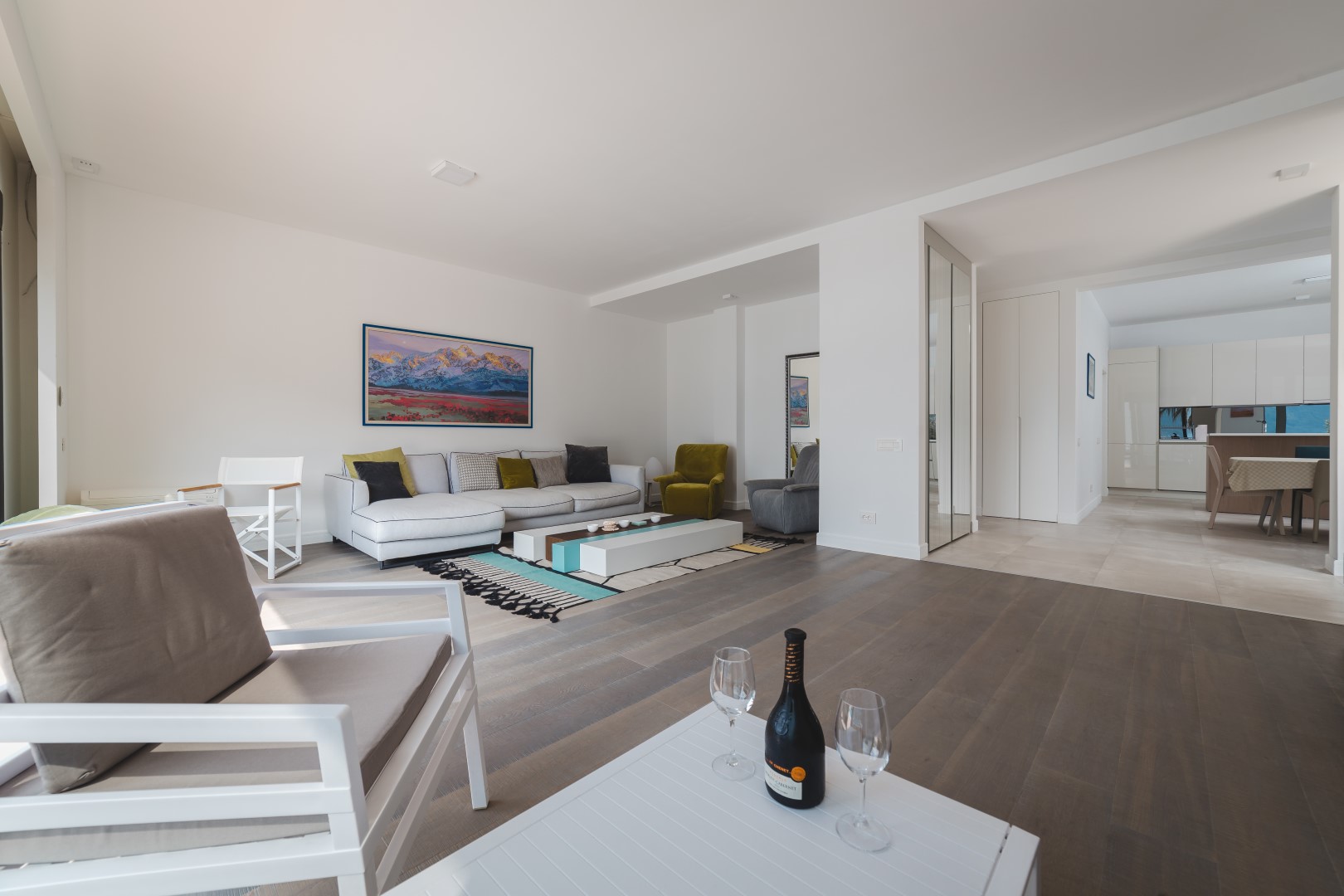 Modern living room with a white sofa and kitchen in a villa in Strp, Montenegro: stylish interior, parquet flooring, and sea view.