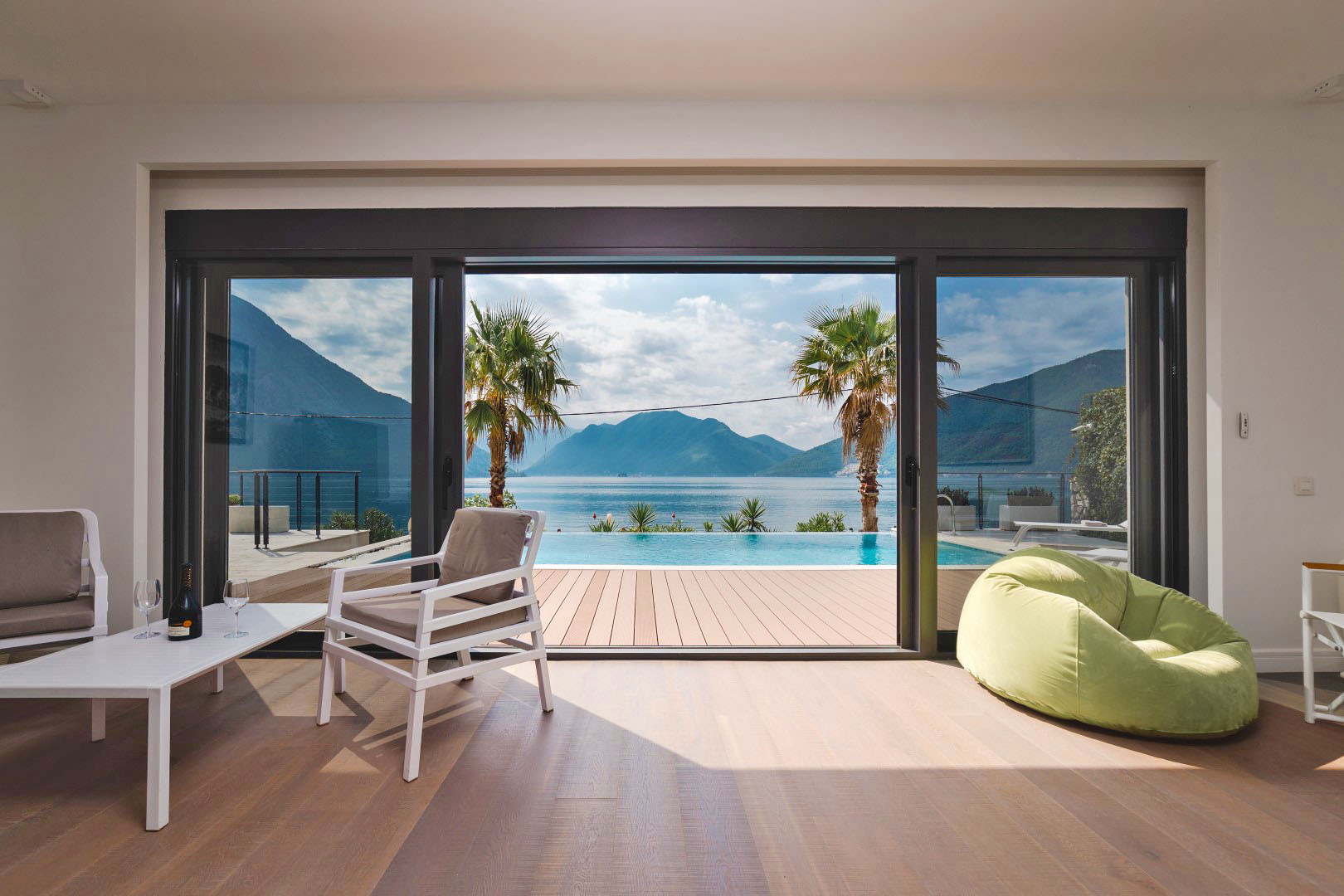 Villa living room in Strp, Montenegro: panoramic windows, sea, pool and mountain views, modern furniture, and a terrace.
