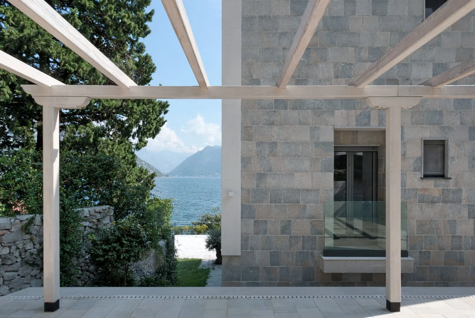 Stone house exterior with a wooden pergola overlooking a lake and mountains.