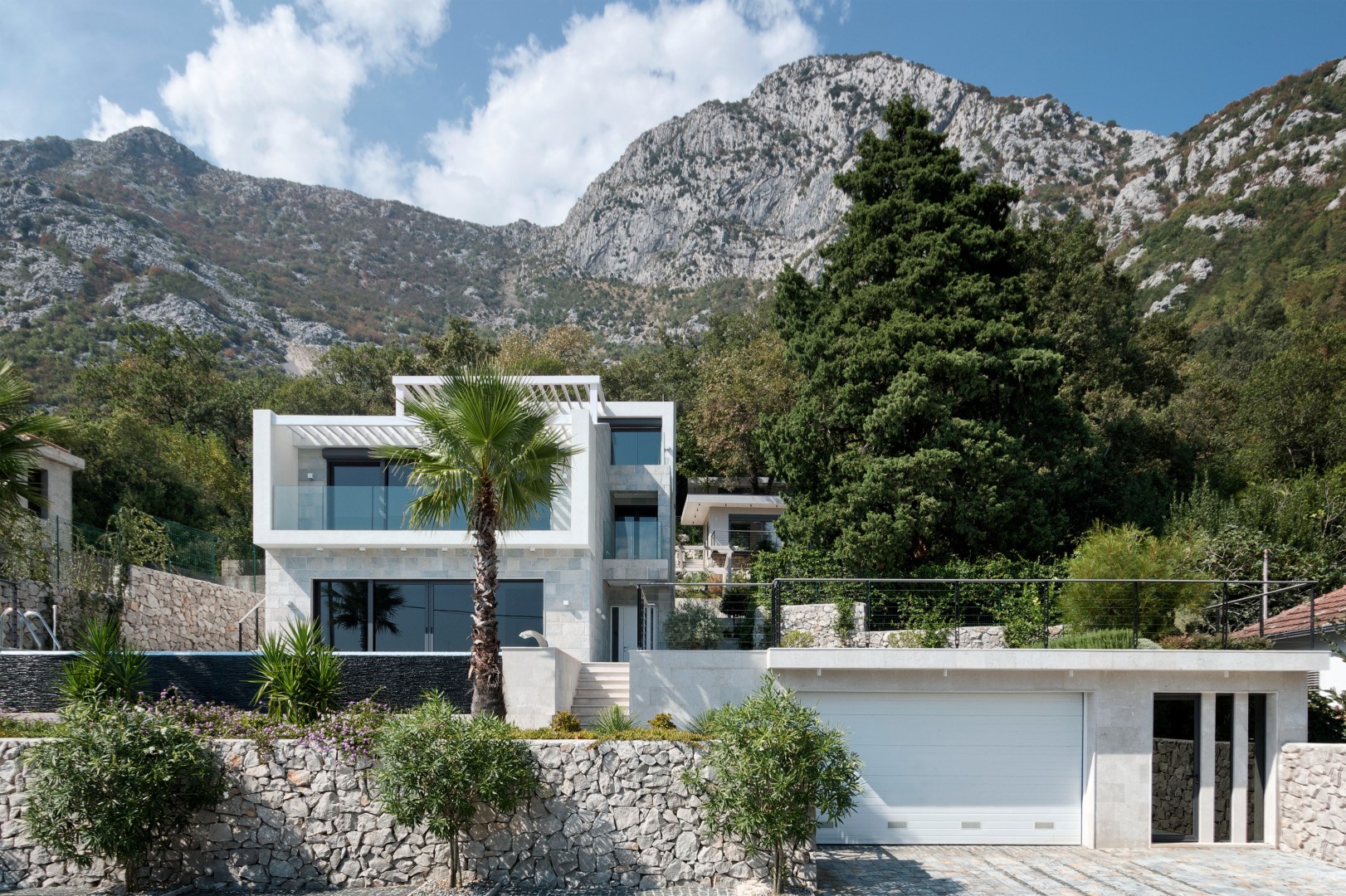 Modern villa in Strp, Montenegro: stone facade, panoramic windows, terrace with pool, and mountain views.