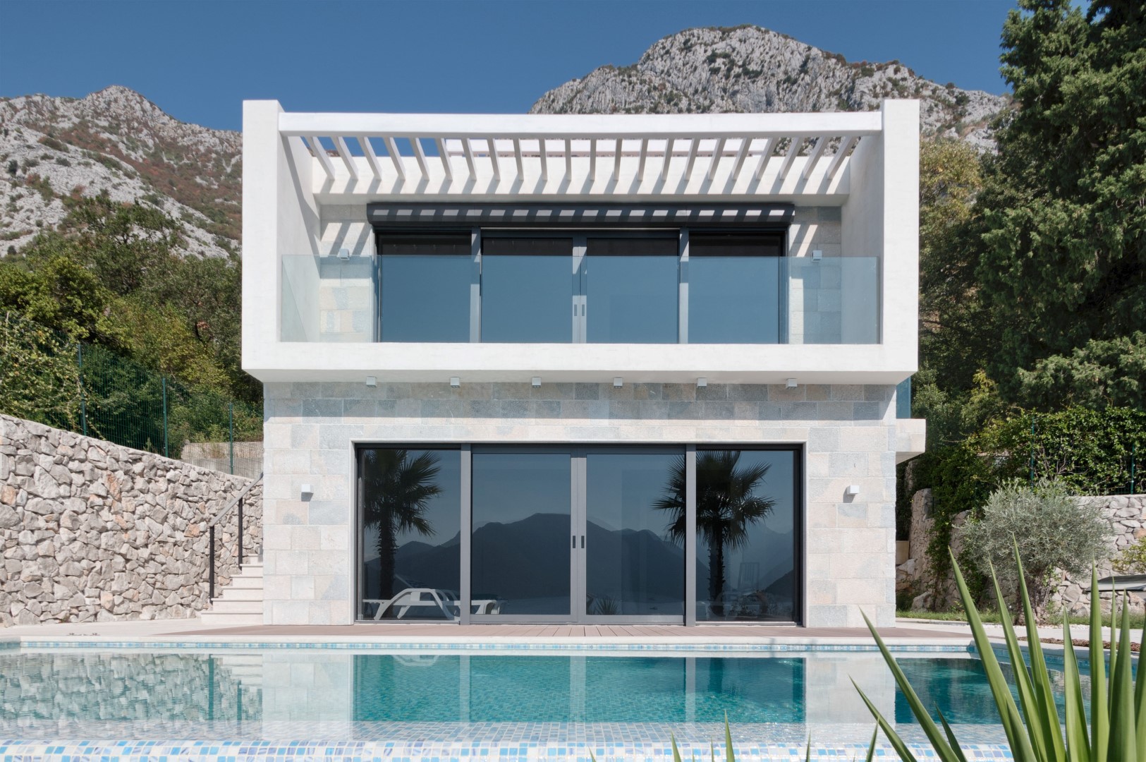 Modern villa in Strp, Montenegro: stone facade, panoramic windows, balcony, and a private pool by the house.