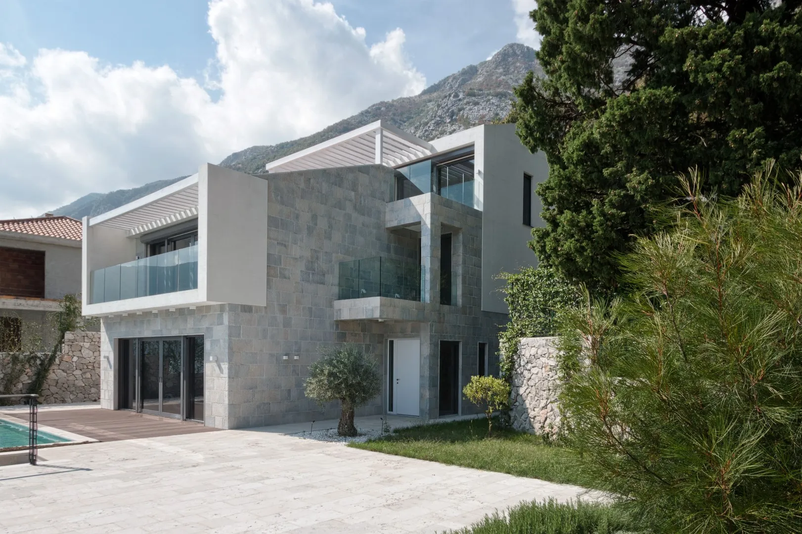 Exterior of a modern stone house with balconies and pool against a mountain backdrop.
