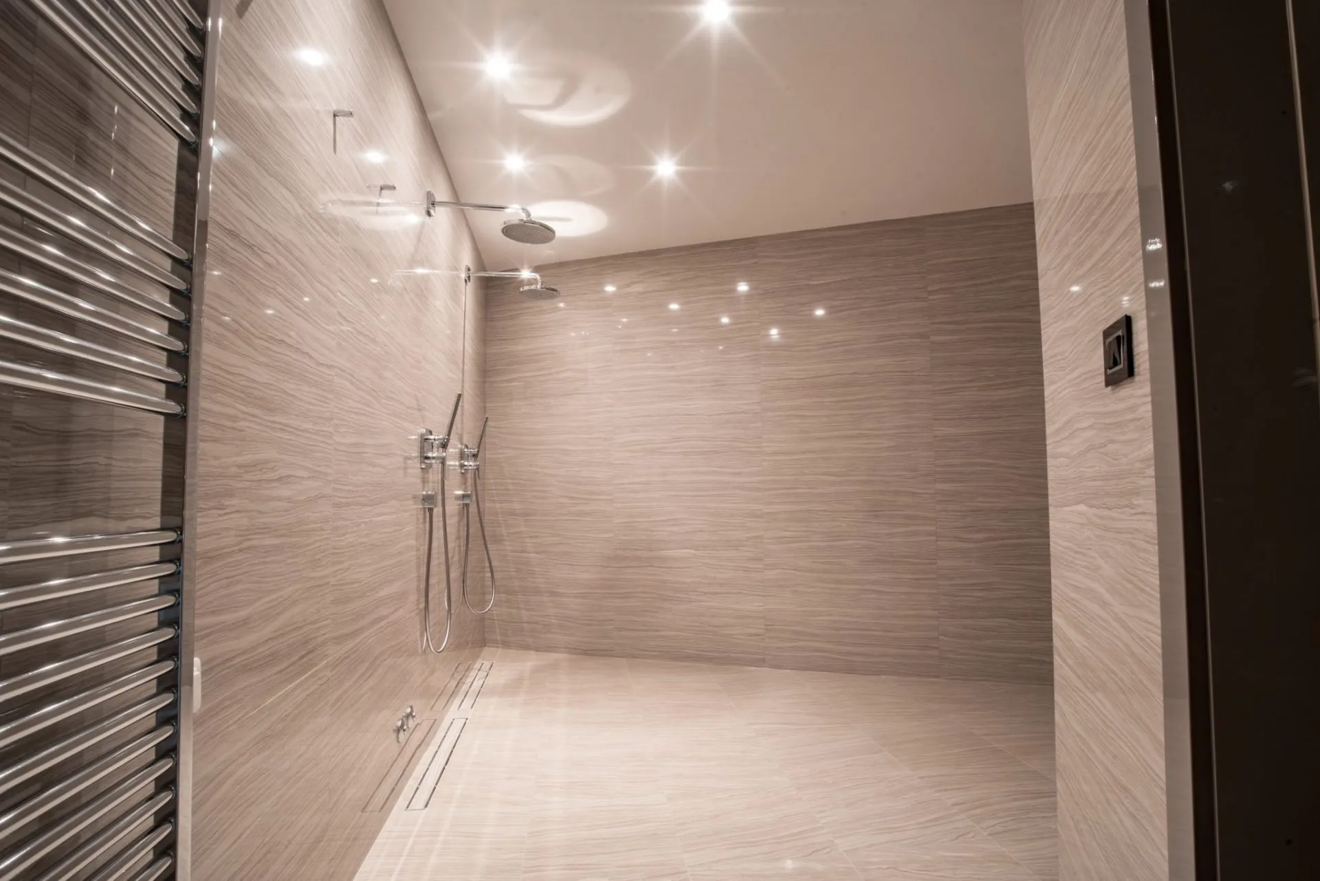 Modern bathroom featuring a walk-in shower with beige stone tiles, dual overhead showers, and a chrome towel warmer.