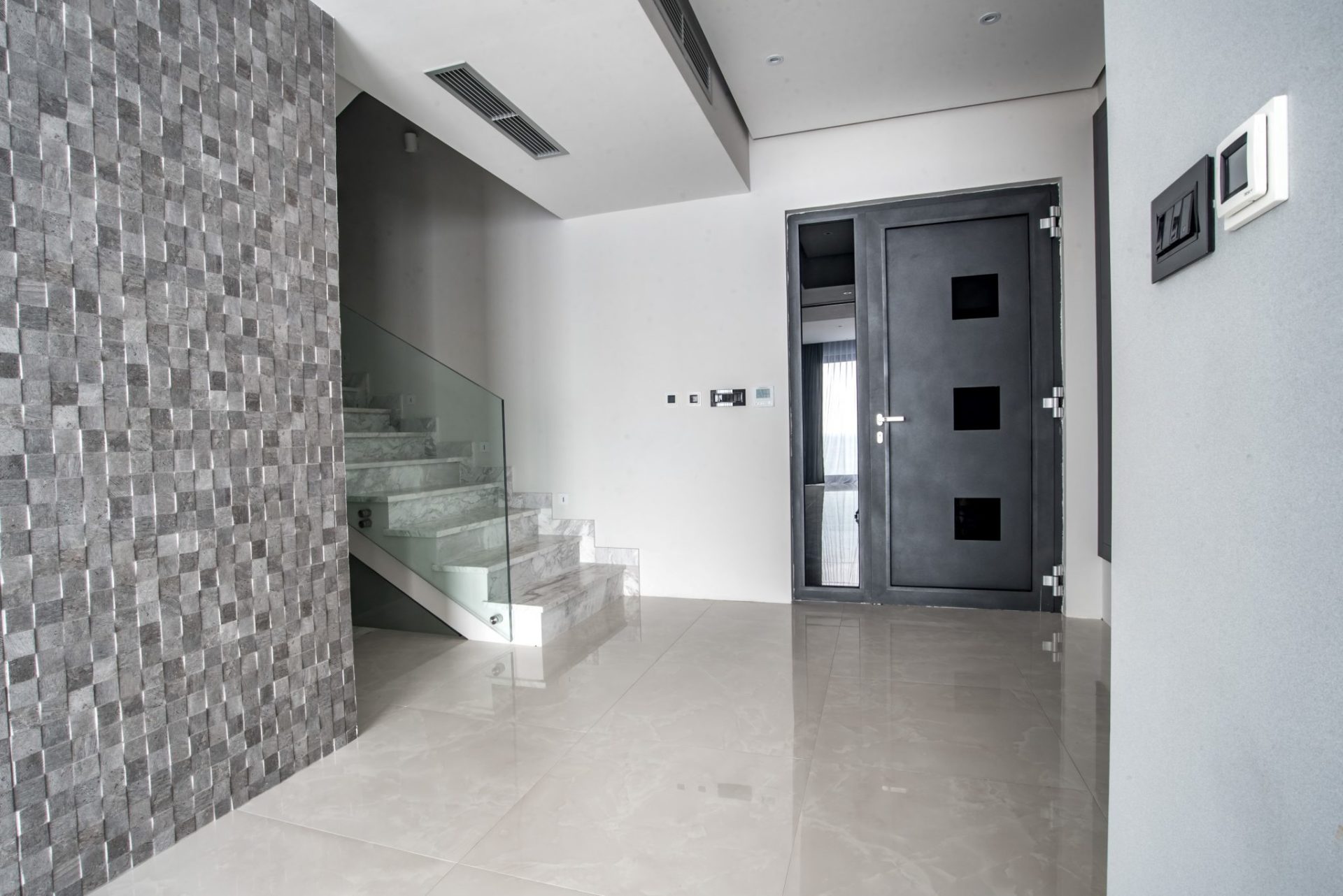 Modern villa interior in Budva, Montenegro: marble staircase with glass railing and a stylish front door.