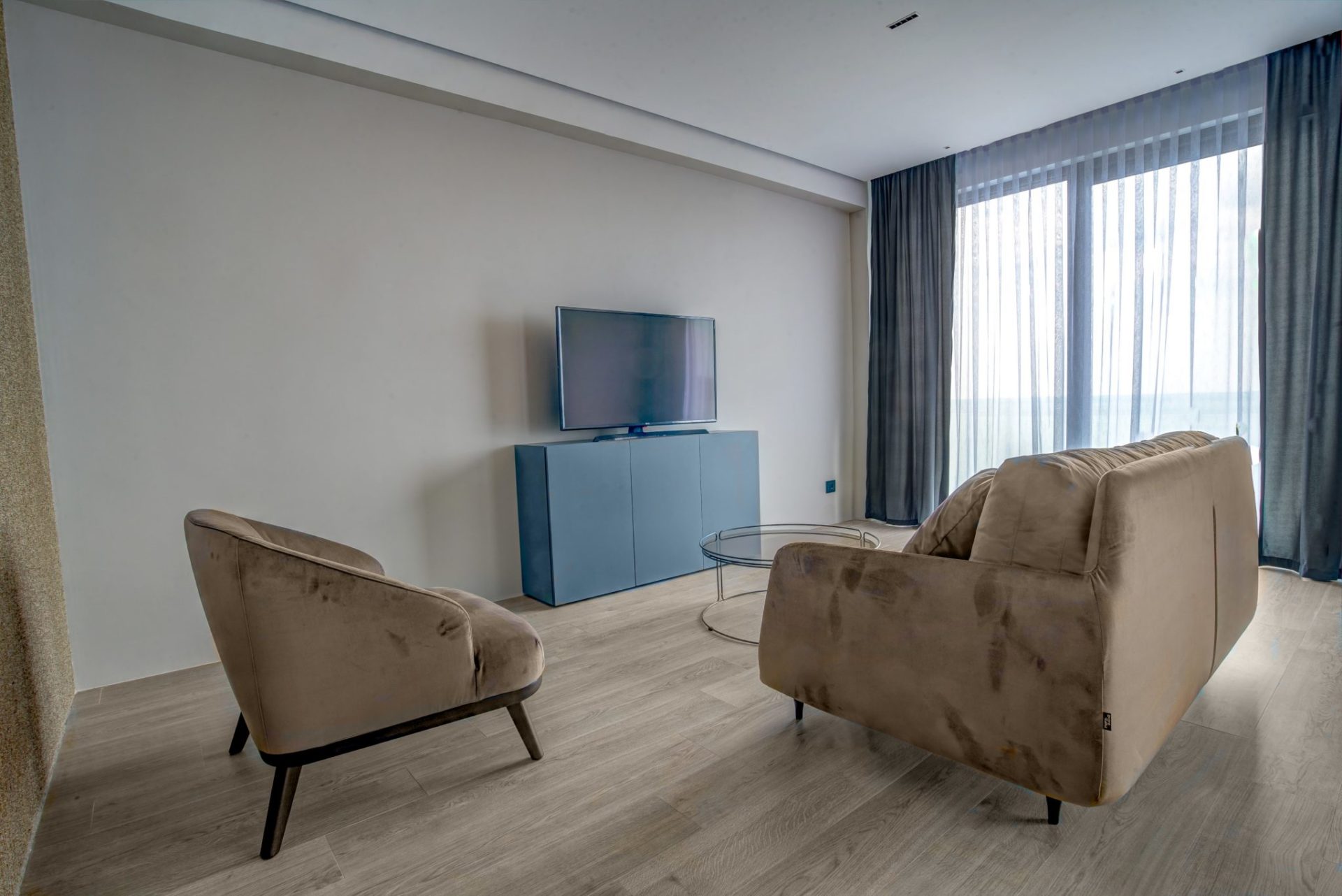 Modern living room with a beige sofa, armchair, and TV area in a villa in Budva, Montenegro. Bright interior with a panoramic view.