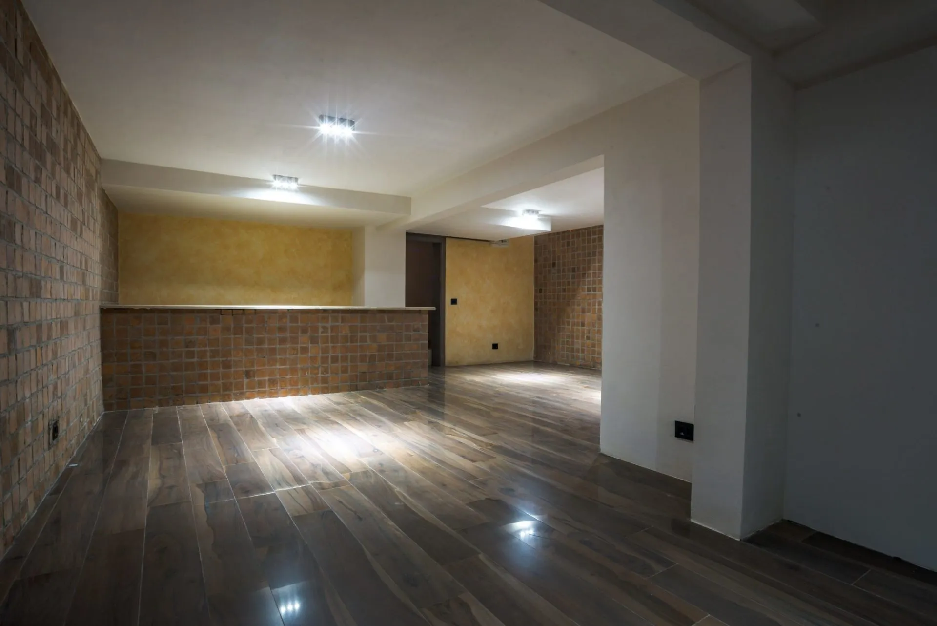 Empty room with wood flooring, exposed brick wall, and low tiled partition walls, no furniture visible.