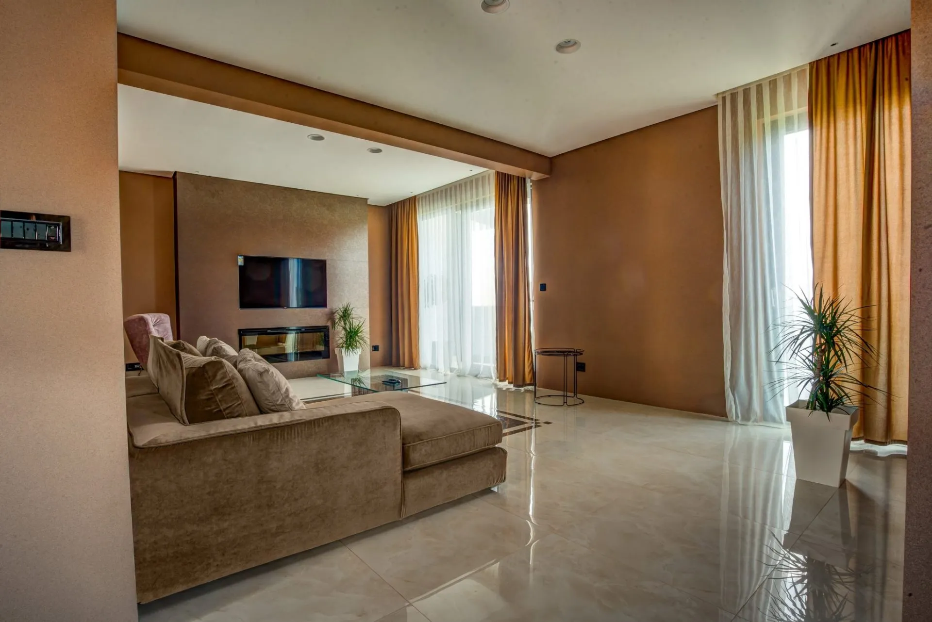 Living room with beige sofa, TV above fireplace, and glossy tiled floors.