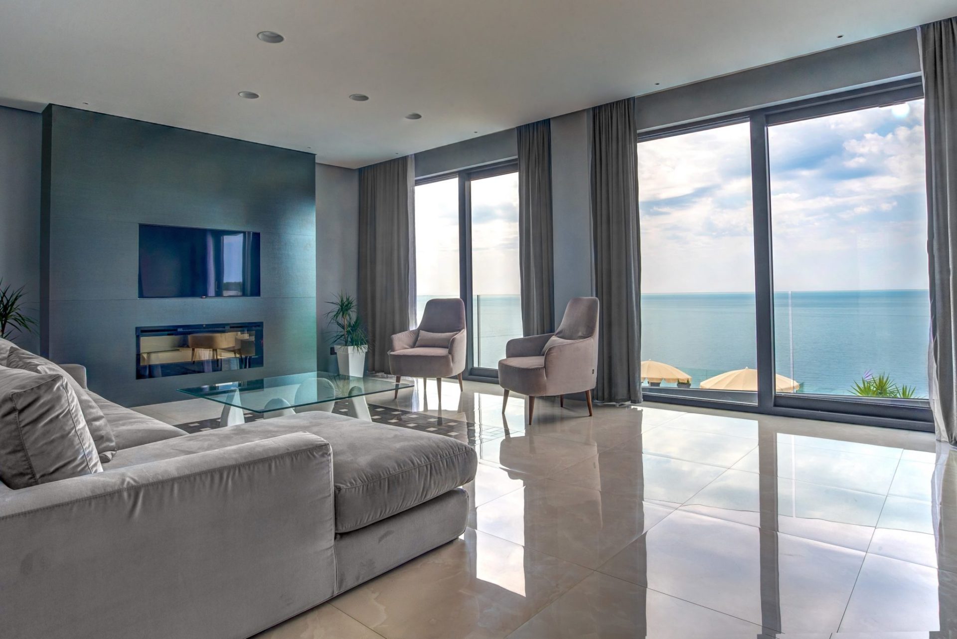 Living room with panoramic sea view in an elite villa, Budva, Montenegro: modern furniture, fireplace, and glass table.