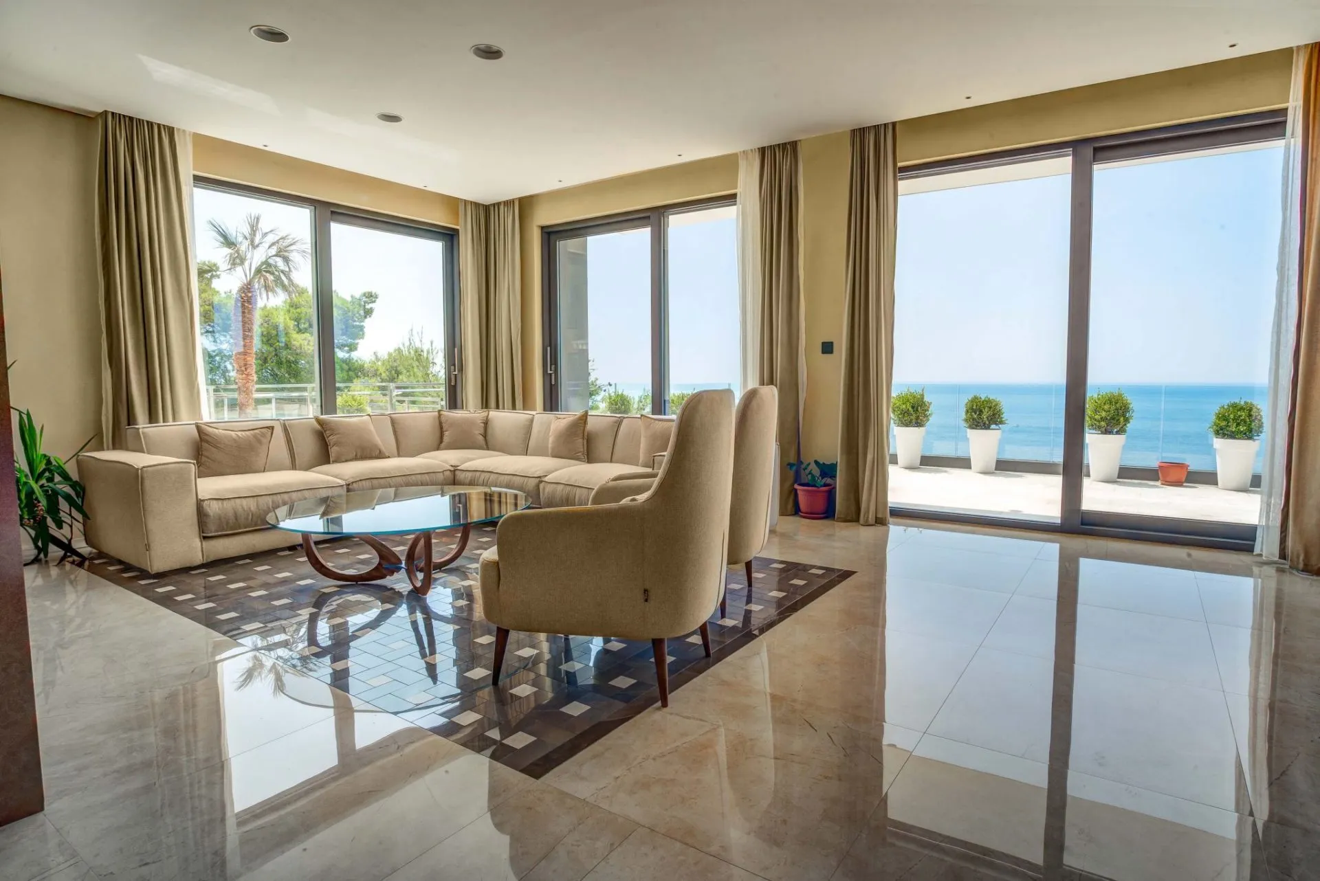 Bright living room with a beige sectional sofa, glass coffee table, and large windows overlooking the ocean.