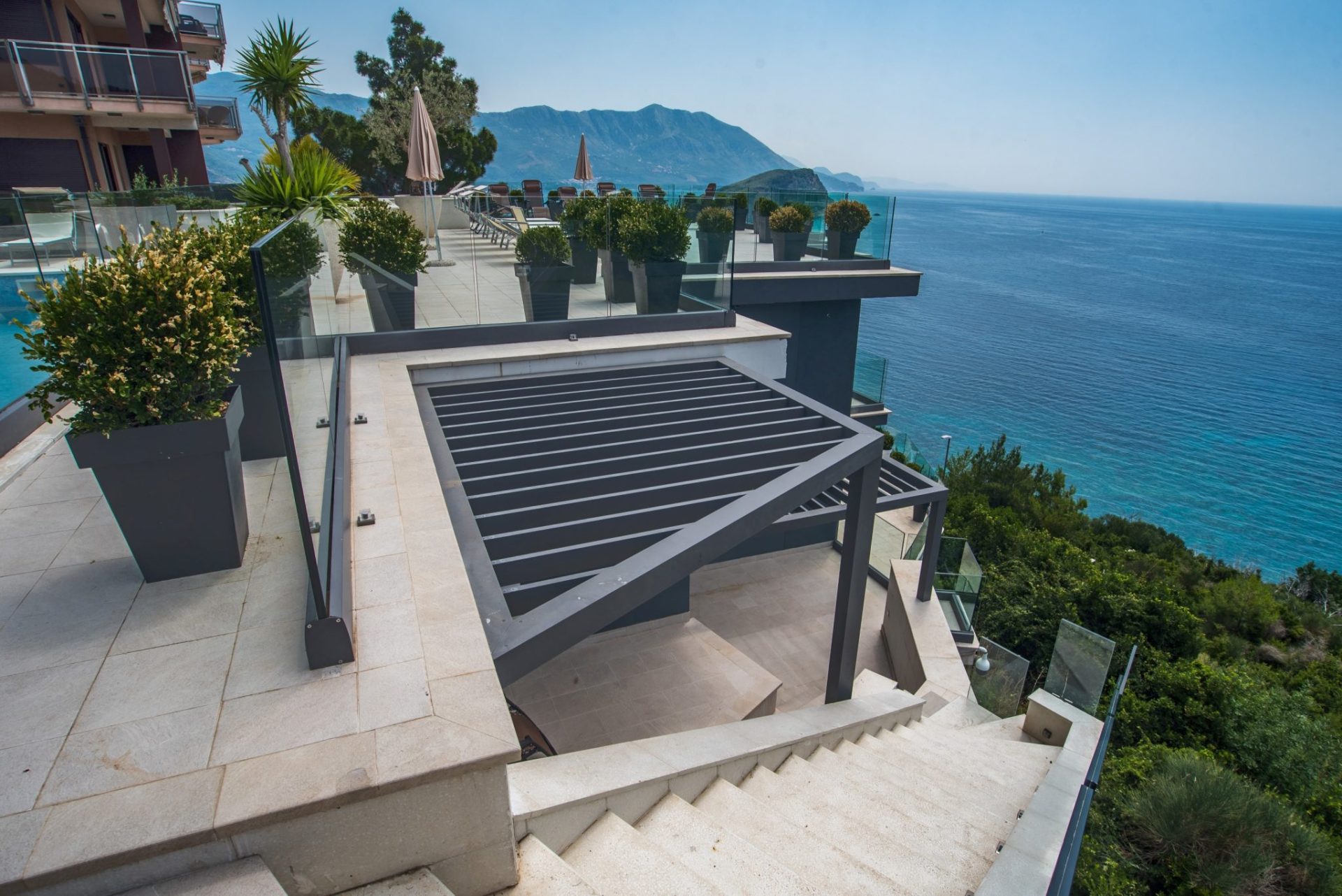 Villa terrace in Budva, Montenegro: panoramic sea view, modern pergola, glass railings, and landscaping.