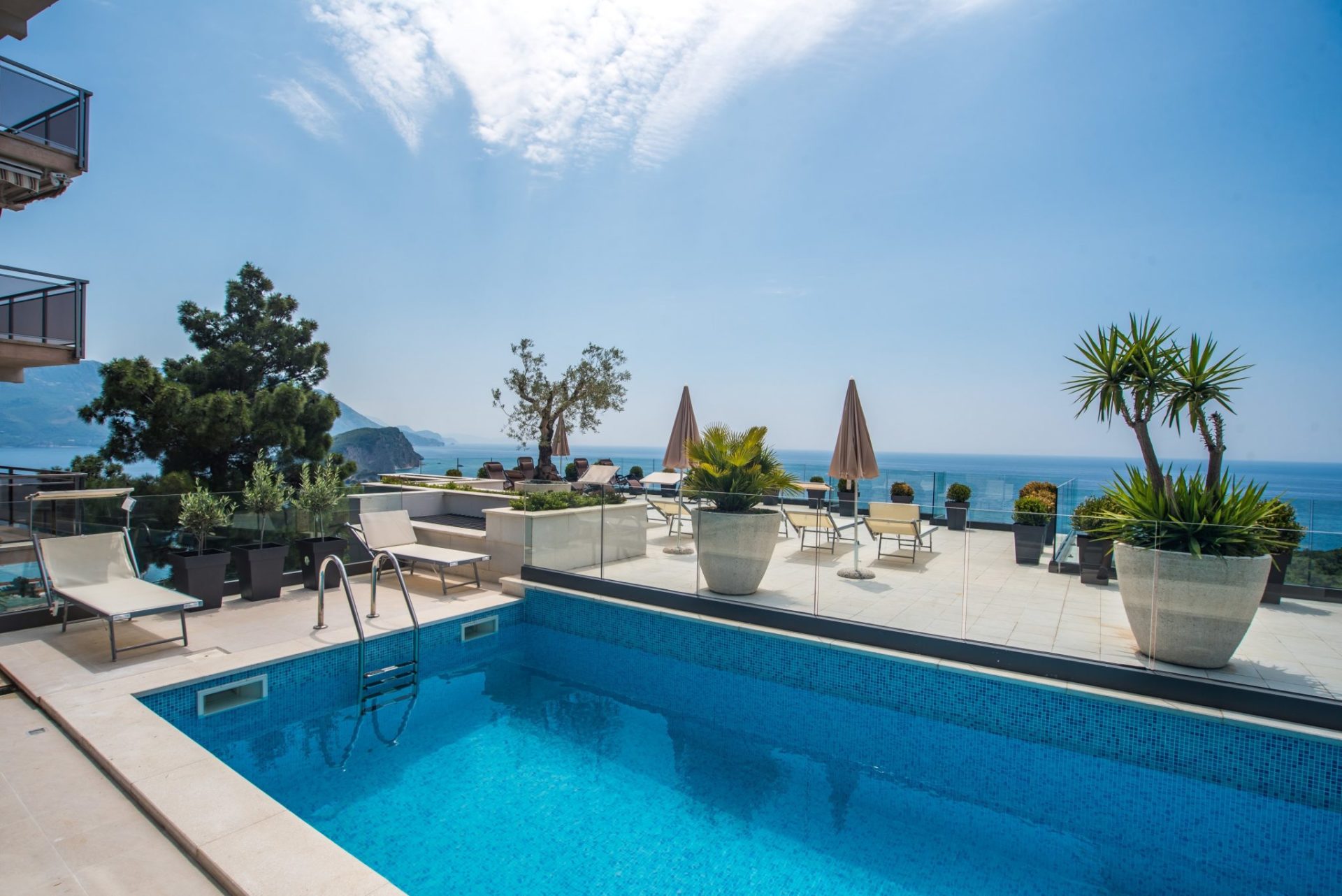 Open-air pool on the villa terrace in Budva, Montenegro, with sun loungers, plants, and panoramic views of the Adriatic Sea.