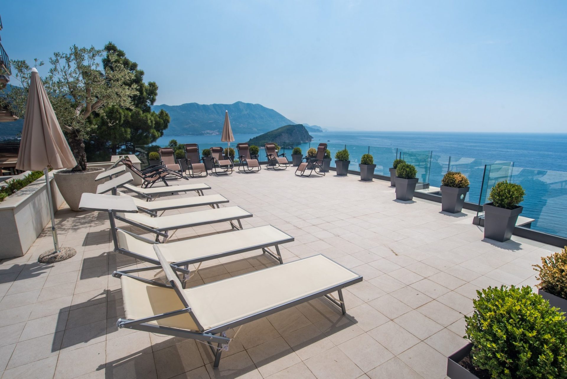 Terrace with loungers and panoramic views of the sea and island in Budva, Montenegro. Modern villa with a lounge area.
