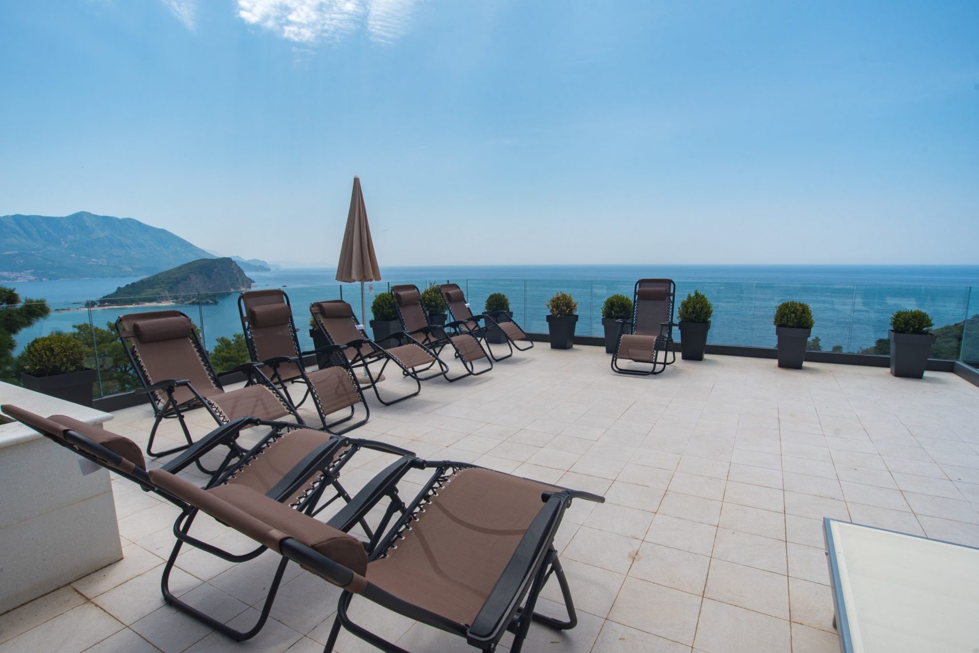 Terrace with sun loungers and panoramic views of the sea and island in Budva, Montenegro. Modern villa with a lounge area.