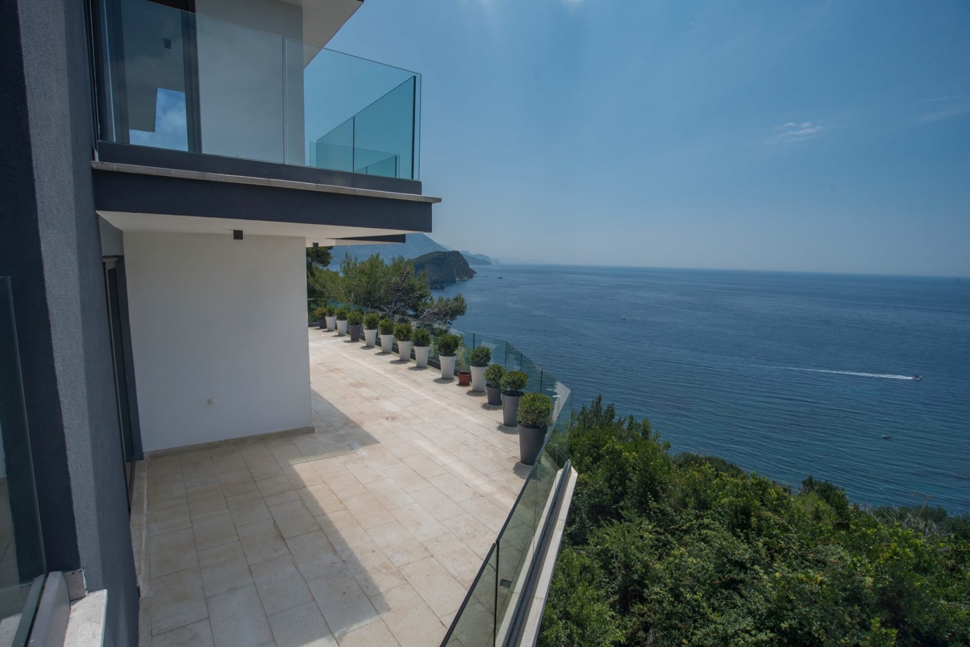 Spacious terrace of a modern villa in Budva, Montenegro, with panoramic sea views and a glass railing.