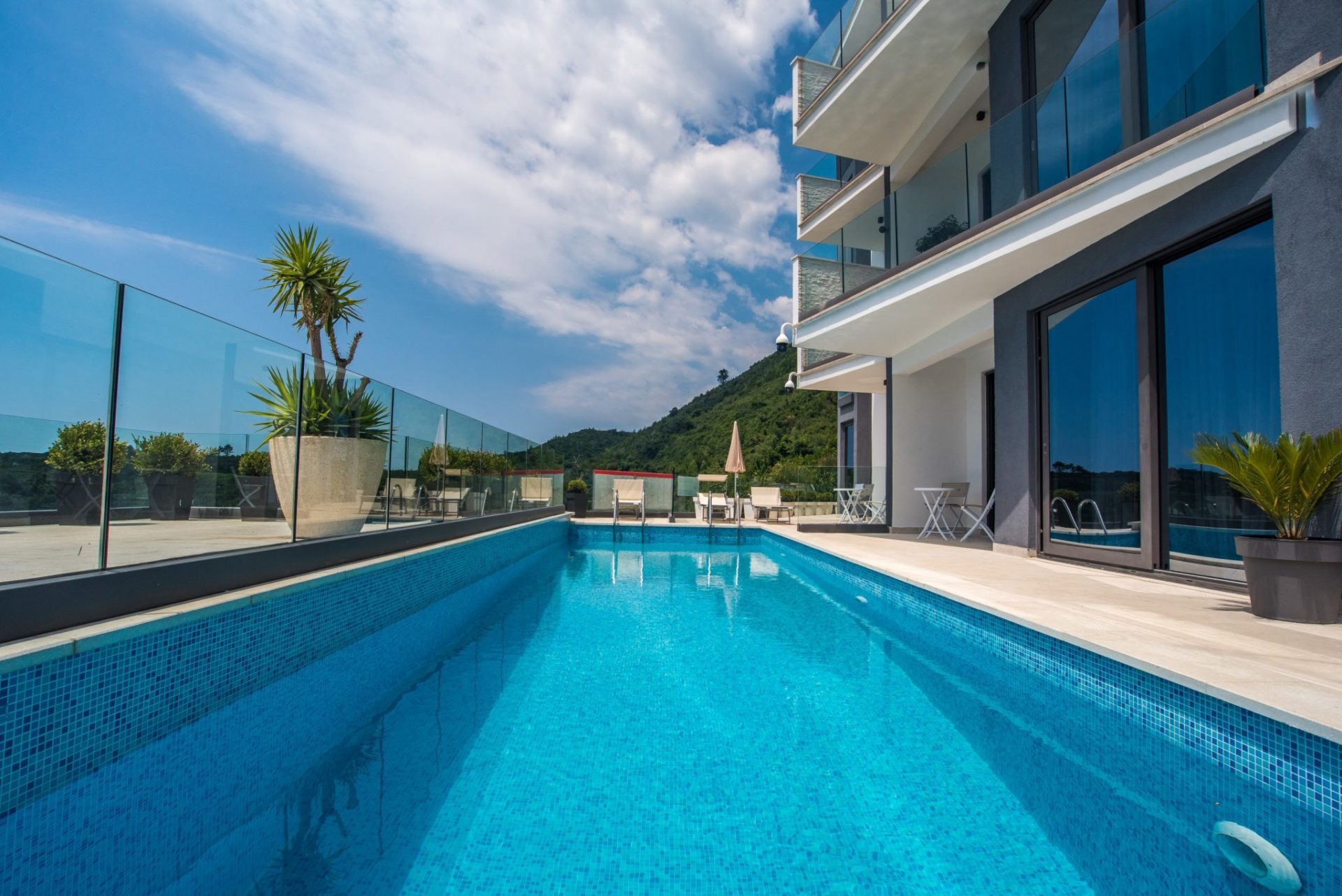 Open-air pool with blue tiles on the terrace of a modern villa in Budva, Montenegro, with mountain views and glass railings.