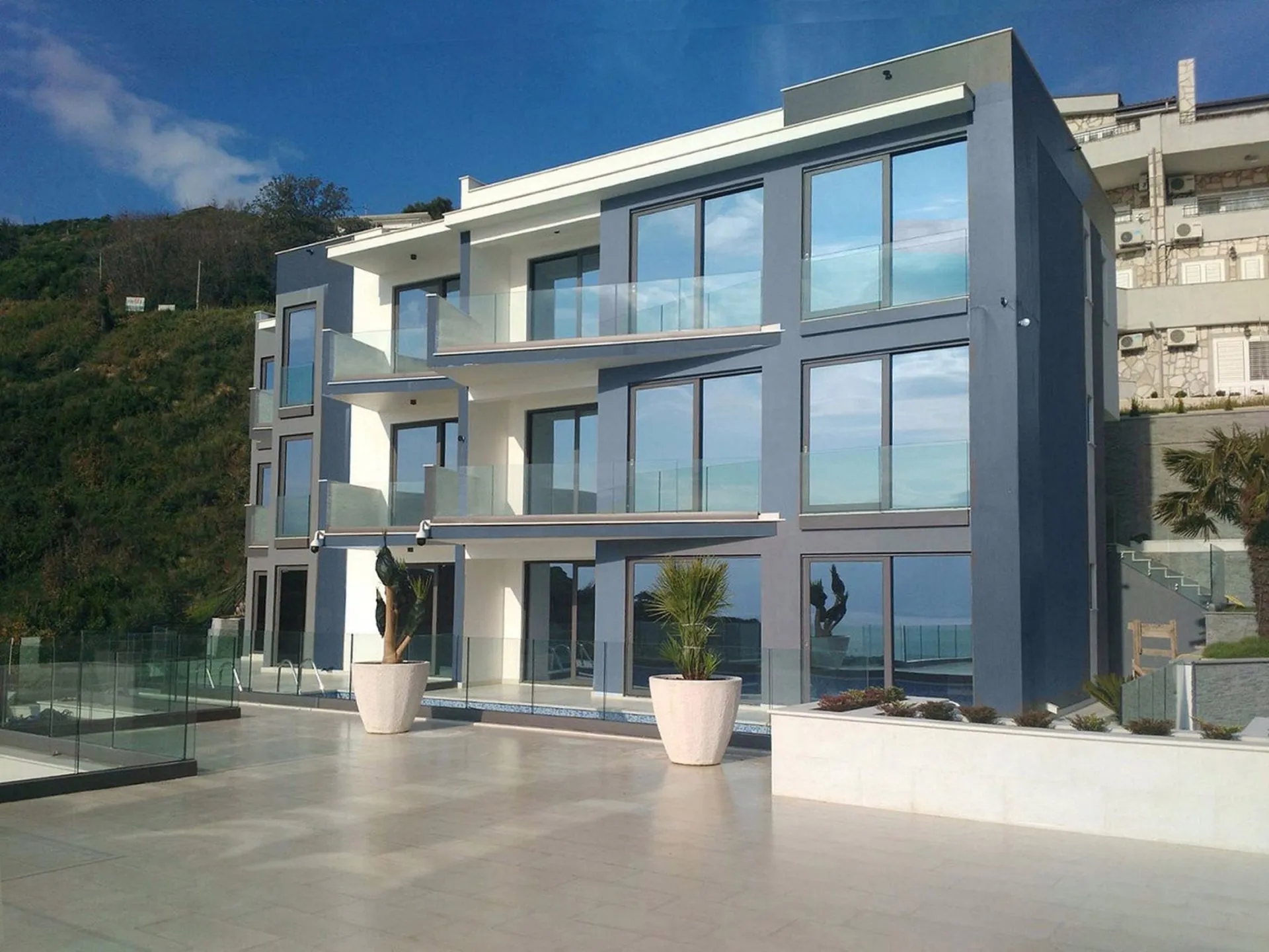 Modern multi-story building with glass balconies and large windows overlooking a hillside.