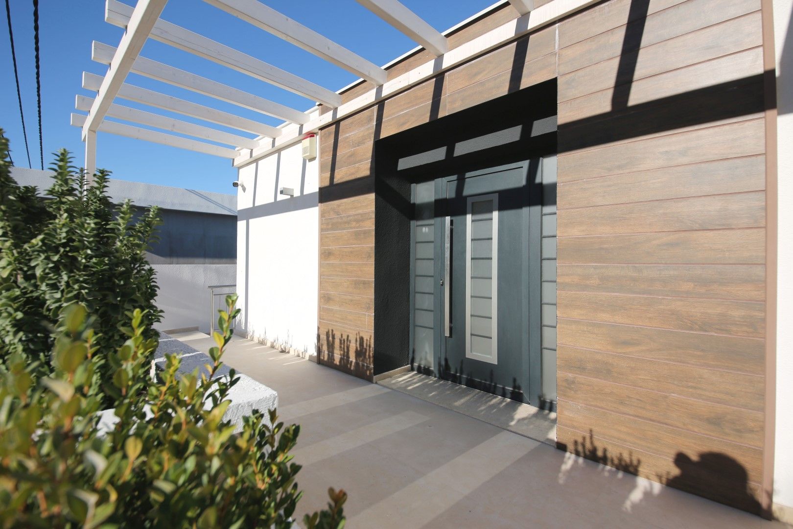 Entrance to a modern villa in Krašići, Montenegro: stylish wood-look facade finish and a terrace with a white pergola.
