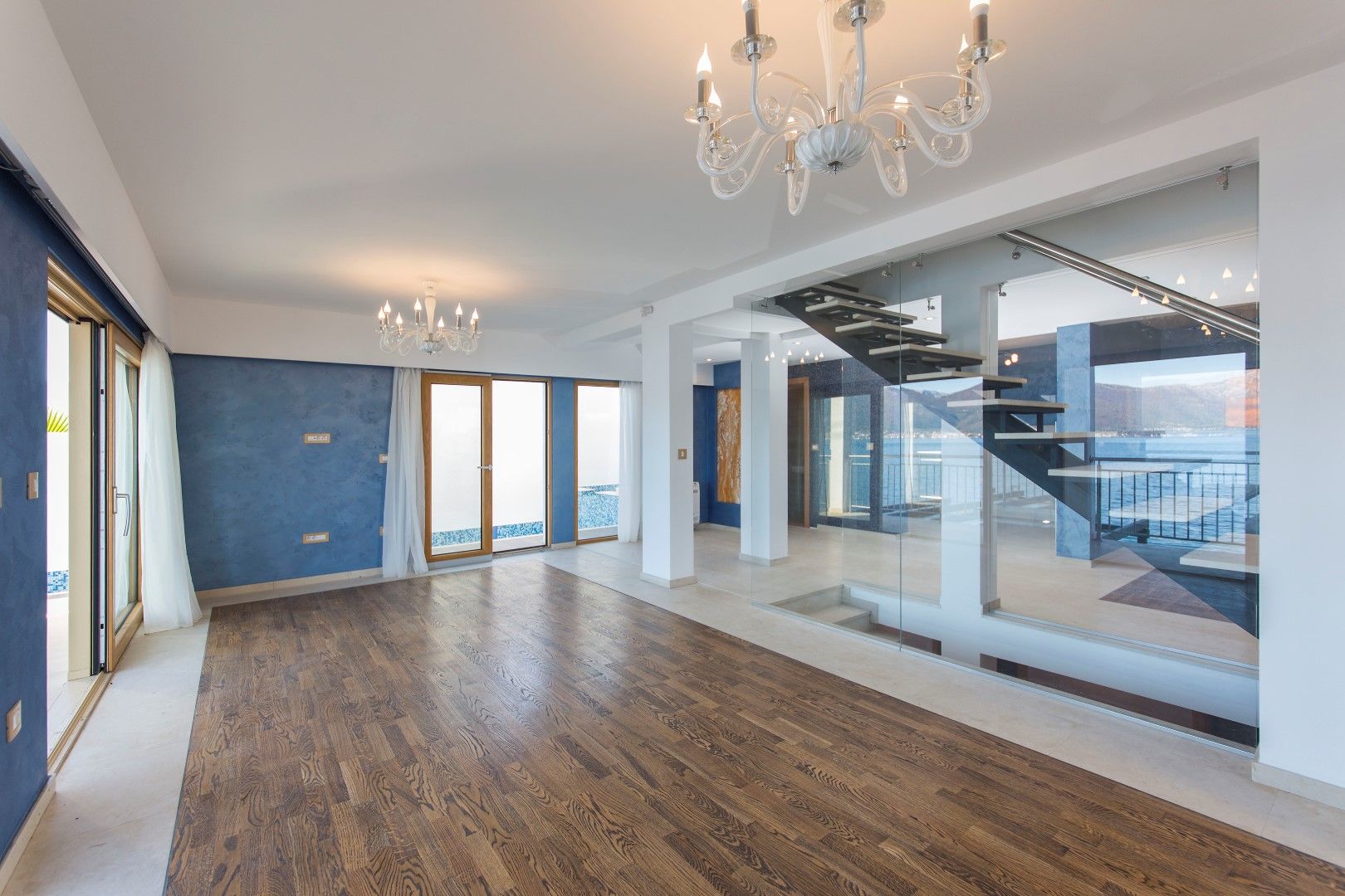 Spacious villa living room in Krašići, Montenegro: wooden floor, glass staircase, and panoramic sea view.