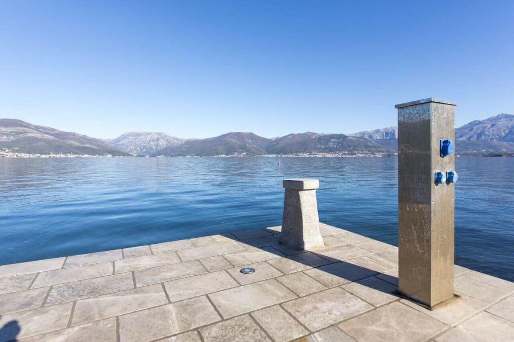Stone pier with a yacht mooring post and panoramic views of the sea and mountains in the village of Krašići, Montenegro.
