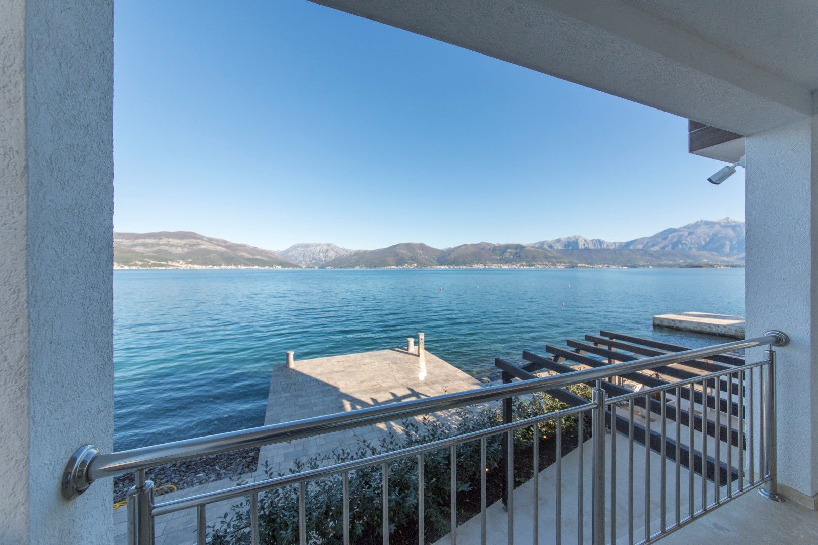 View from the villa balcony in Krašići, Montenegro: a panorama of the sea, mountains, and a private pier by the water.