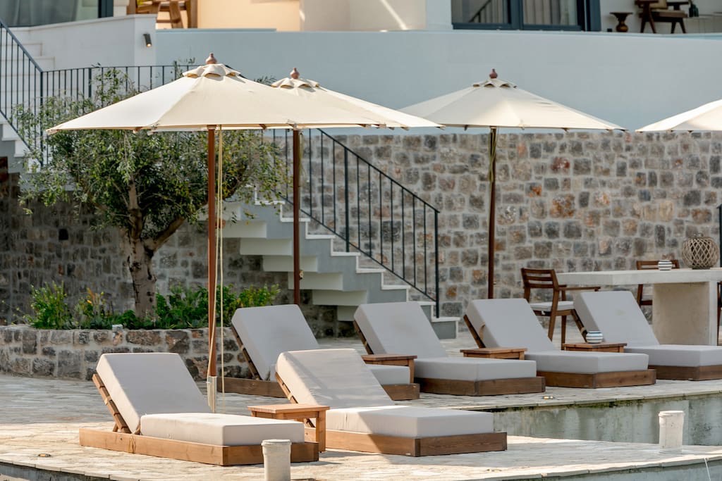 Poolside relaxation area at a villa in Luštica, Montenegro: sun loungers, umbrellas, and stone facade detailing.