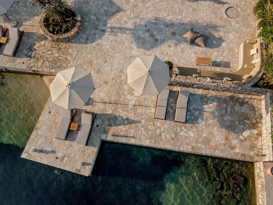 Villa terrace on the first line in Luštica, Montenegro: pool, sun loungers, umbrellas, and a lounge area with stone finishes.