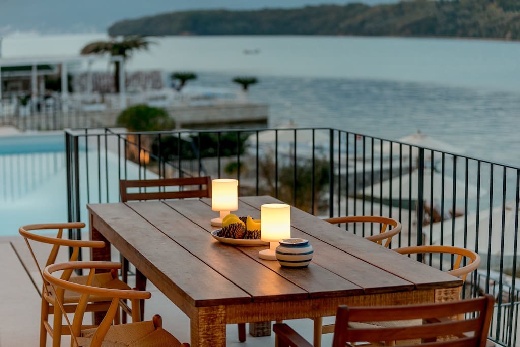 Villa terrace in Luštica, Montenegro: wooden table, sea view, and a pool on the beachfront.