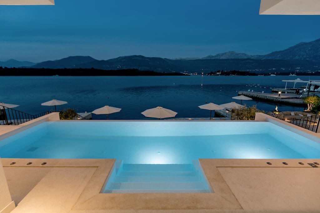 Infinity pool with lighting at a villa in Lustica, Montenegro, with panoramic sea and mountain views in the evening.
