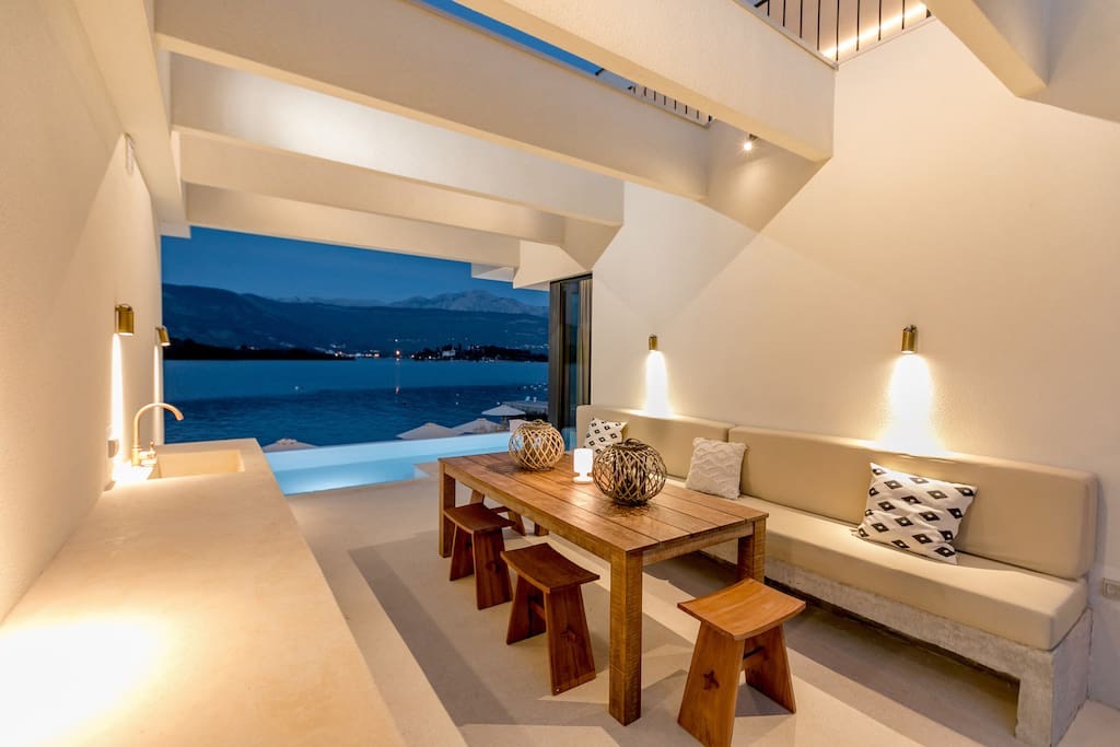 Villa terrace in Luštica, Montenegro: dining area with a wooden table, sea view, and a beachfront pool.