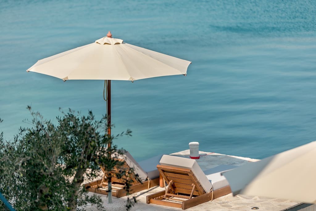 Sun loungers and an umbrella on the private beach of a beachfront villa in Luštica, Montenegro, overlooking the Adriatic Sea.