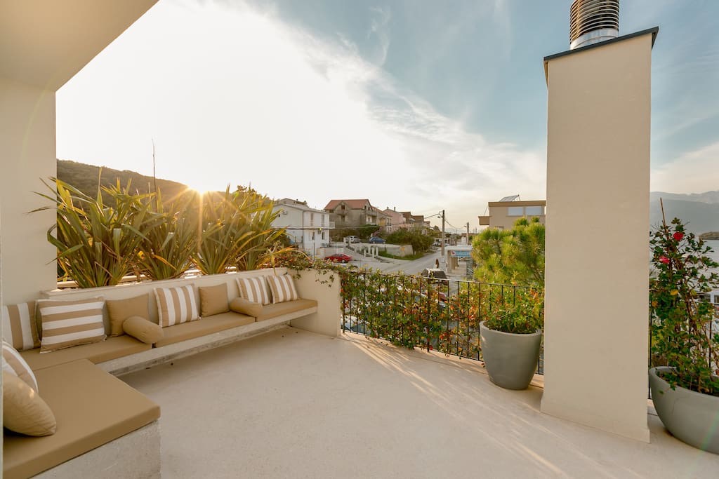 Spacious villa terrace in Luštica, Montenegro: built-in seating with cushions, plants, and a view of the coastline.