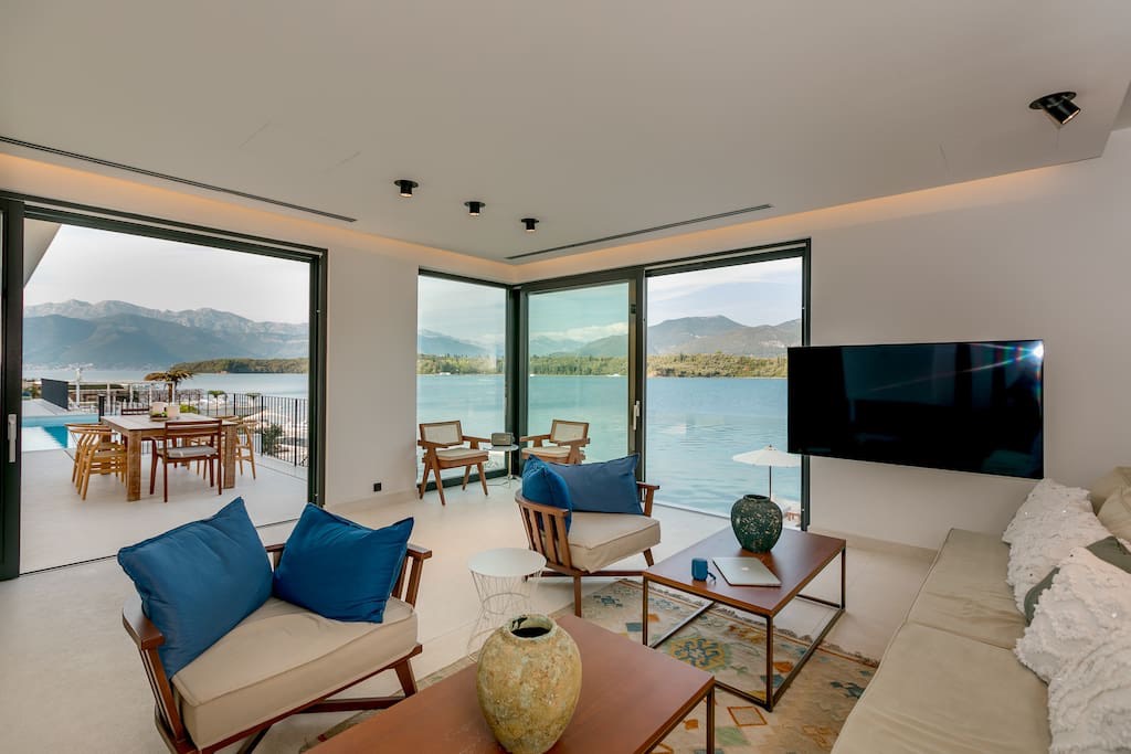 Villa living room in Luštica, Montenegro: panoramic windows with sea views, modern furniture, and a terrace with a pool.