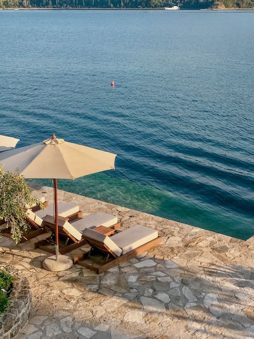 Private villa terrace on the seafront in Luštica, Montenegro: sun loungers, an umbrella, and direct access to the Adriatic Sea.