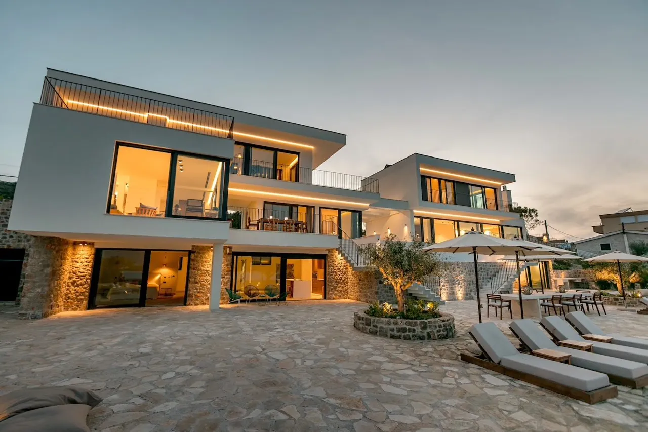 Modern house exterior with stone patio, terrace, and sun loungers at dusk.