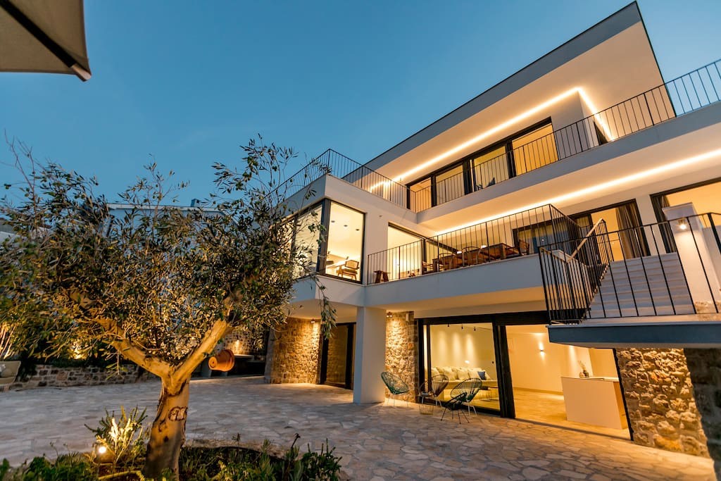 Modern villa in Luštica, Montenegro: illuminated facade, stone cladding, terrace, and an olive tree in the yard.