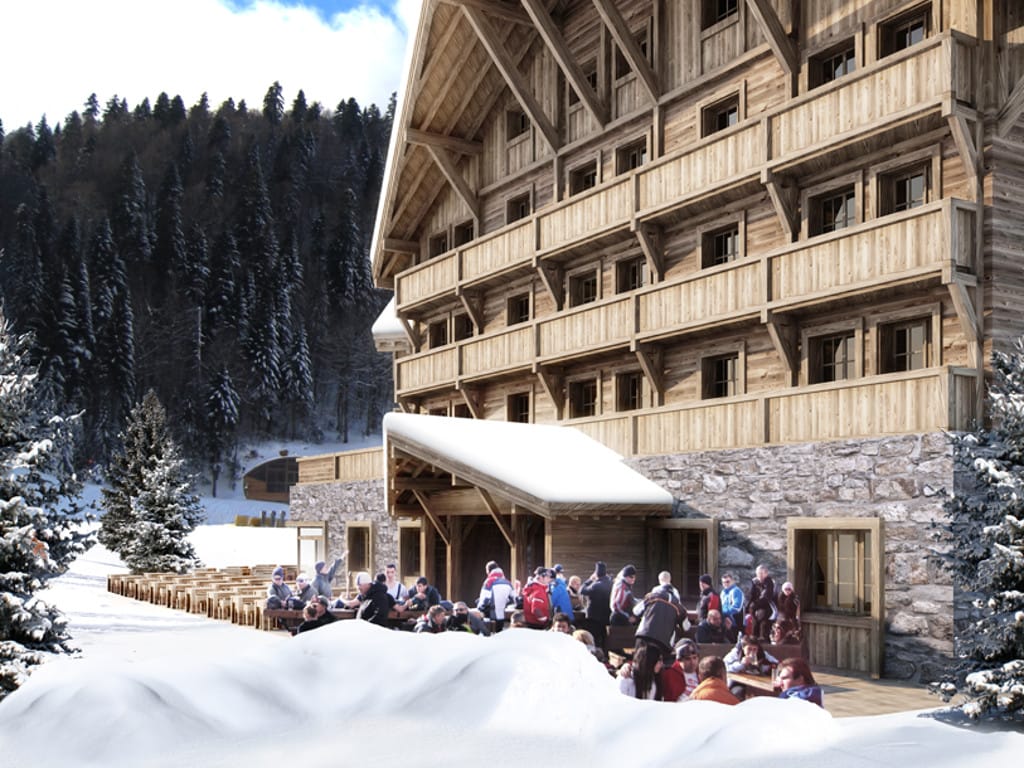 Facade of a mountain hotel in Kolašin, Montenegro: wood cladding, stone base, and a terrace with guests against a forest backdrop.
