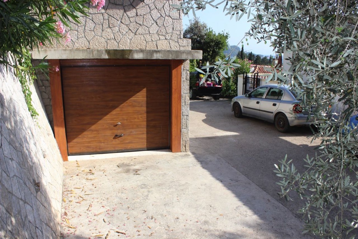 Garage with brown doors and parking by a villa in Budva, Montenegro: stone facade and an olive tree.