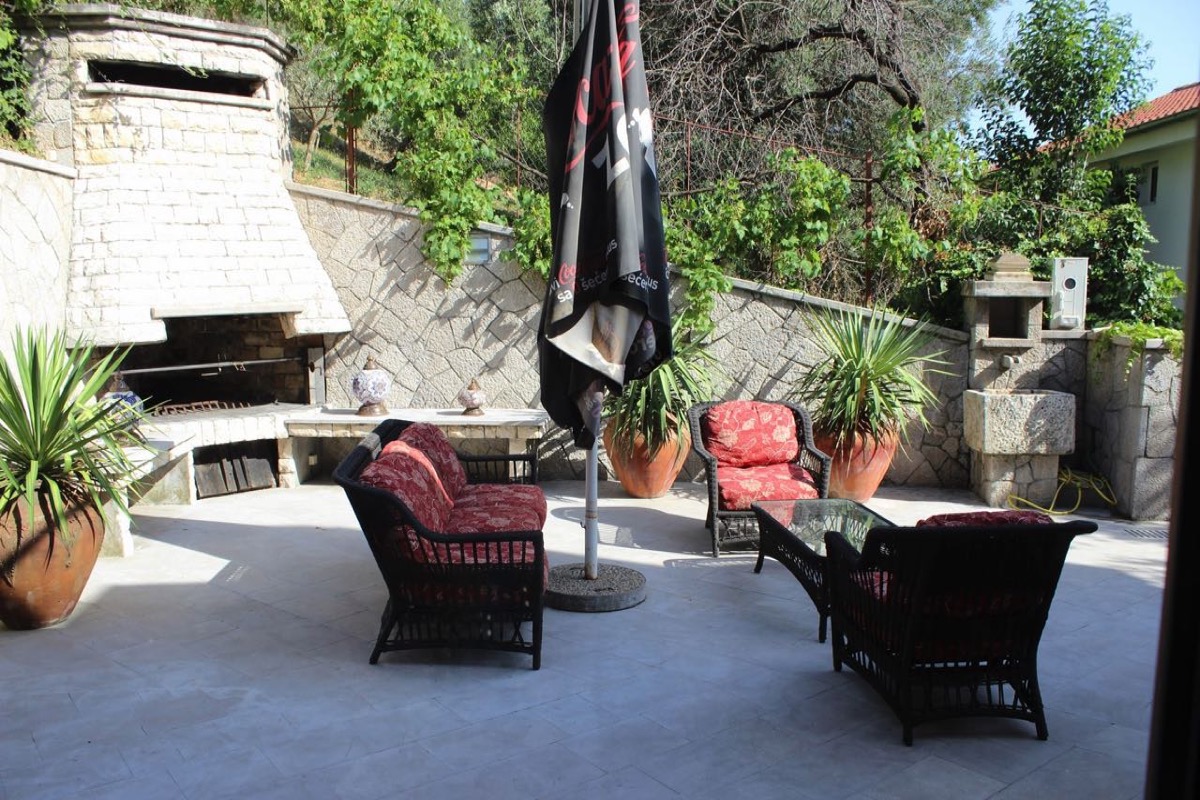 Villa terrace in Budva, Montenegro: a relaxation area with wicker furniture, a stone barbecue, and a Mediterranean-style garden.