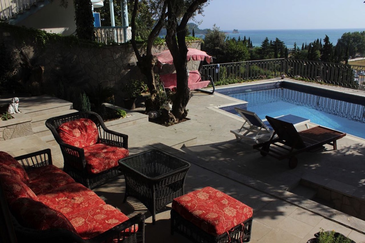 Villa terrace in Budva, Montenegro: pool, wicker furniture with red cushions, and panoramic sea view.