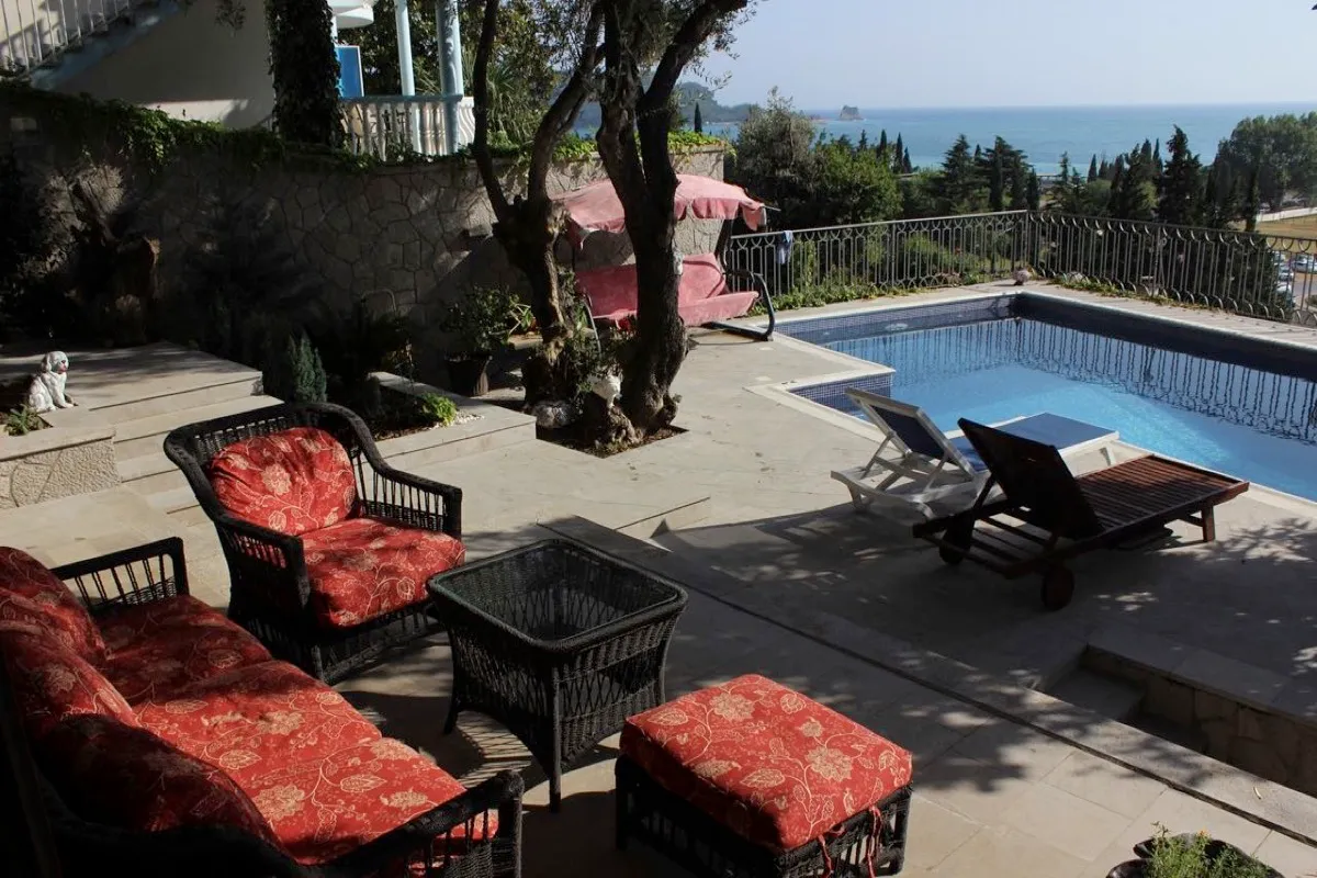 Outdoor terrace with a swimming pool, red furniture, and sea view.