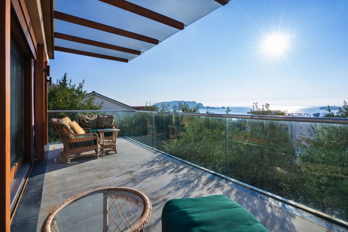 Spacious villa terrace in Budva, Montenegro, with wicker furniture, glass railing, and panoramic sea views.