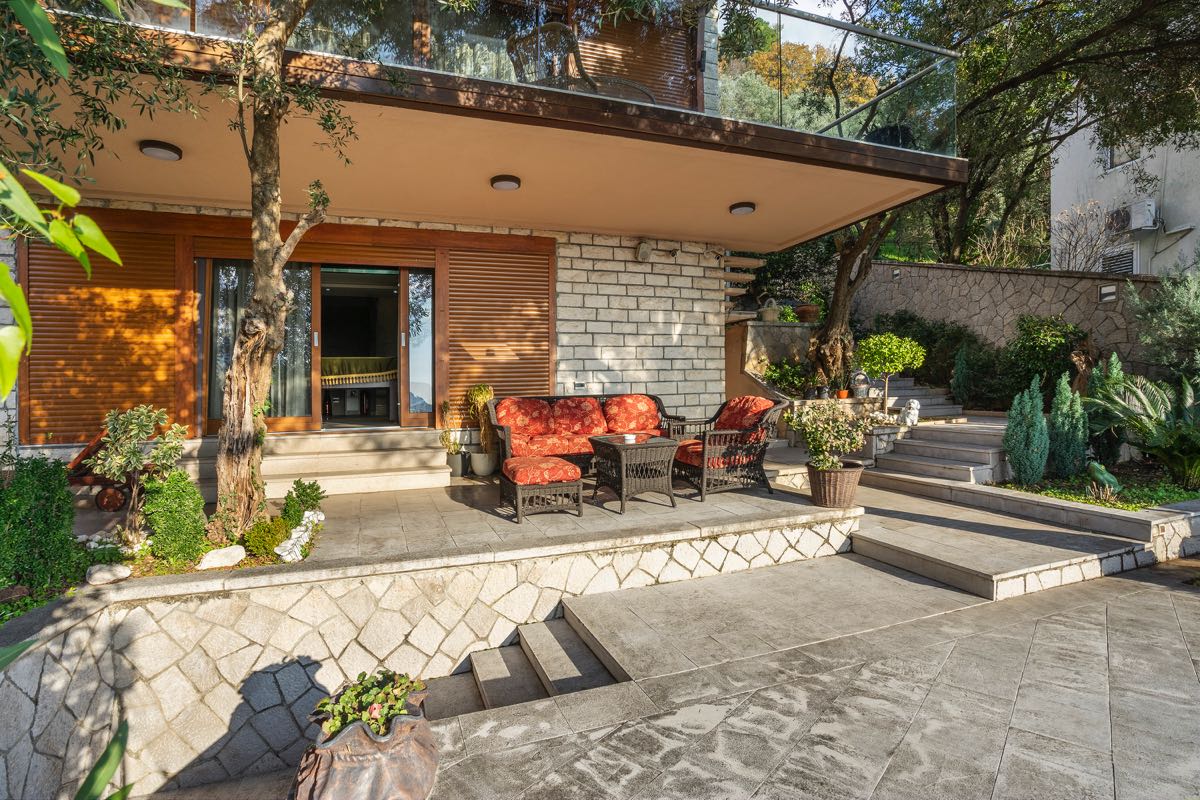 Villa terrace in Budva, Montenegro: stone finish, wicker furniture with red cushions, and landscaping.