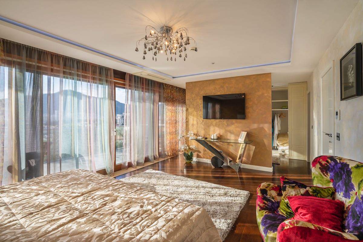 Bedroom with panoramic windows in a villa in Budva, Montenegro: designer furniture, TV, and walk-in closet area.