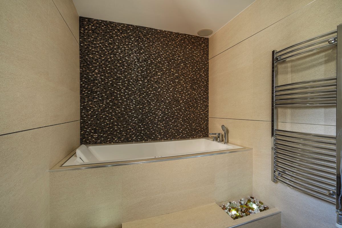 Modern bathroom in a villa in Budva, Montenegro: built-in bathtub, mosaic tiles, and a towel warmer.