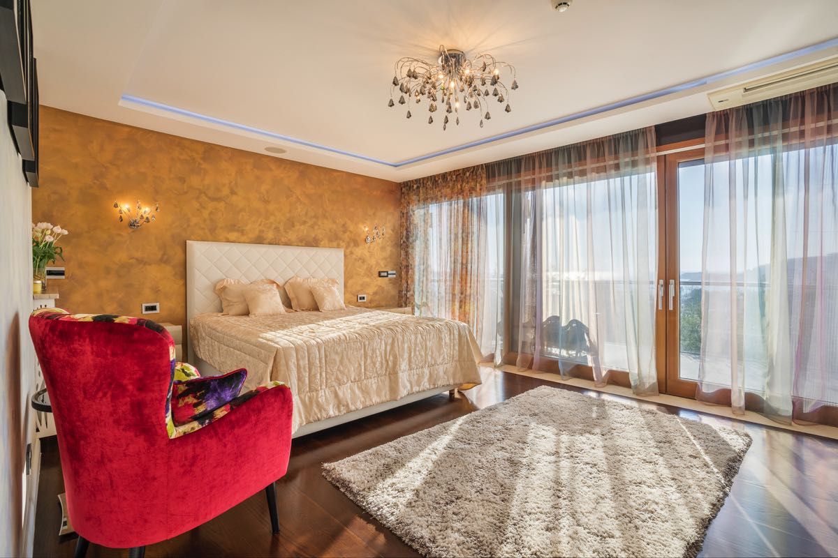 Bedroom with a double bed, a red armchair, and panoramic windows in a villa in Budva, Montenegro.